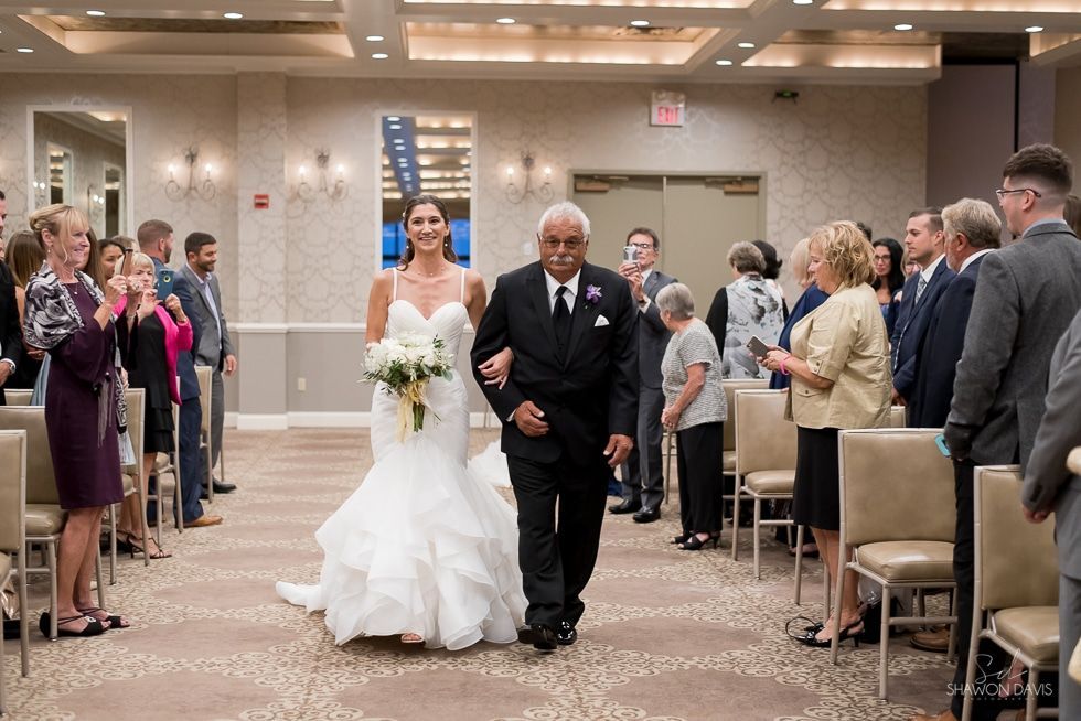 Bride and older man walking down aisle at indoor wedding ceremony with guests standing on both sides