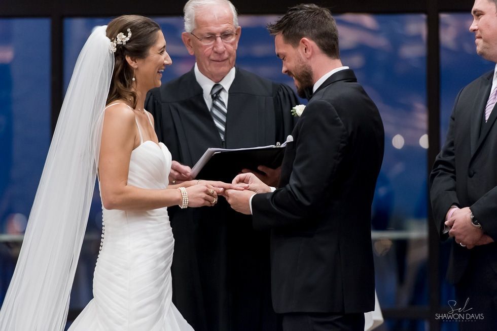 Bride and groom exchange vows during a wedding ceremony, with an officiant holding a book.