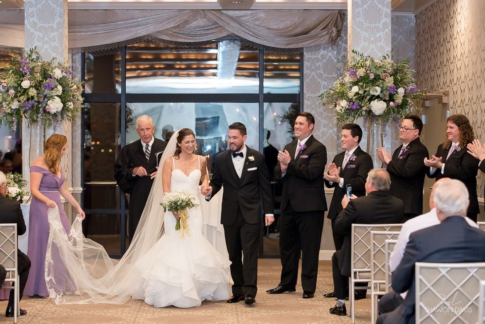 Wedding ceremony with bride and groom at the altar, surrounded by bridal party and guests in a decorated hall