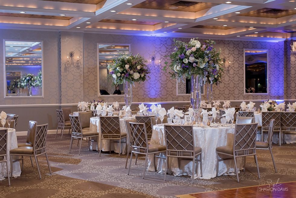 Elegant banquet hall with round tables, white linens, floral centerpieces, and soft blue uplighting.