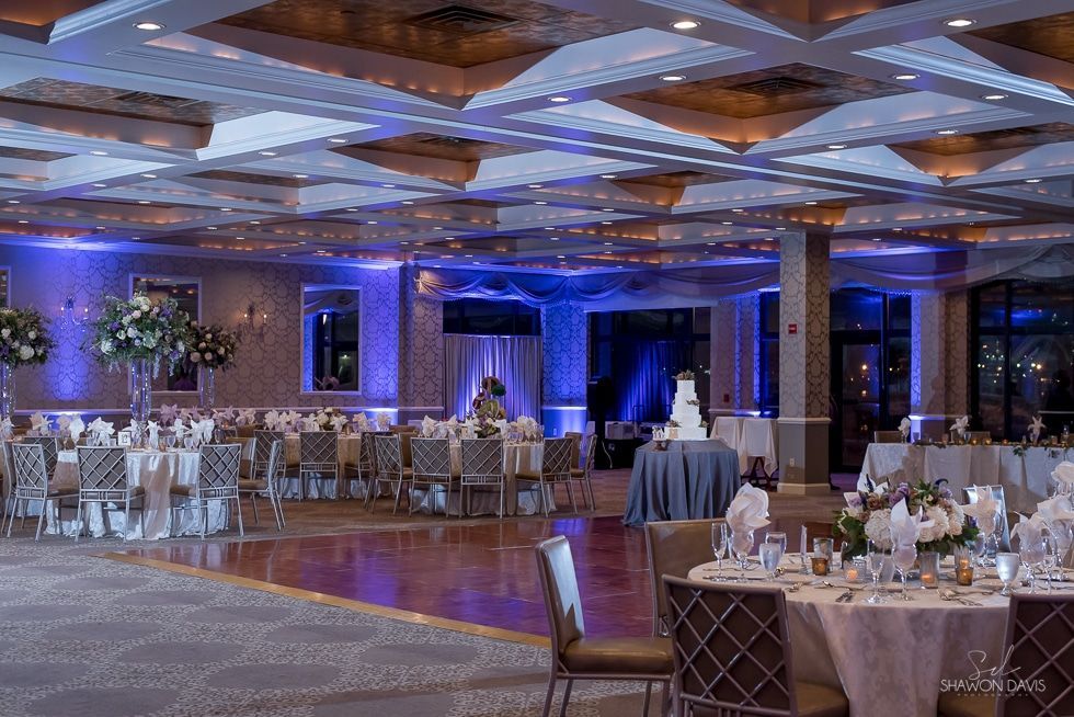 Elegant banquet hall with round, set tables and blue-lit mirrored ceiling before an event