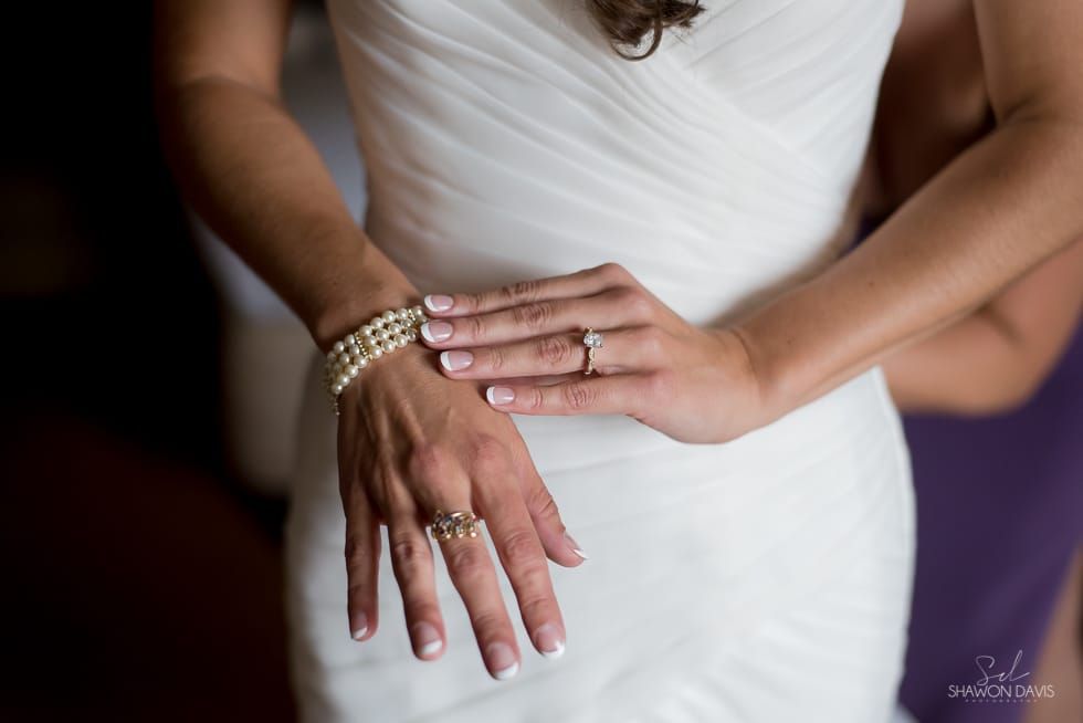 Two hands with wedding rings resting on a white wedding dress