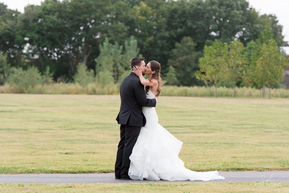 Couple in formal attire embracing on a grassy field with trees in the background