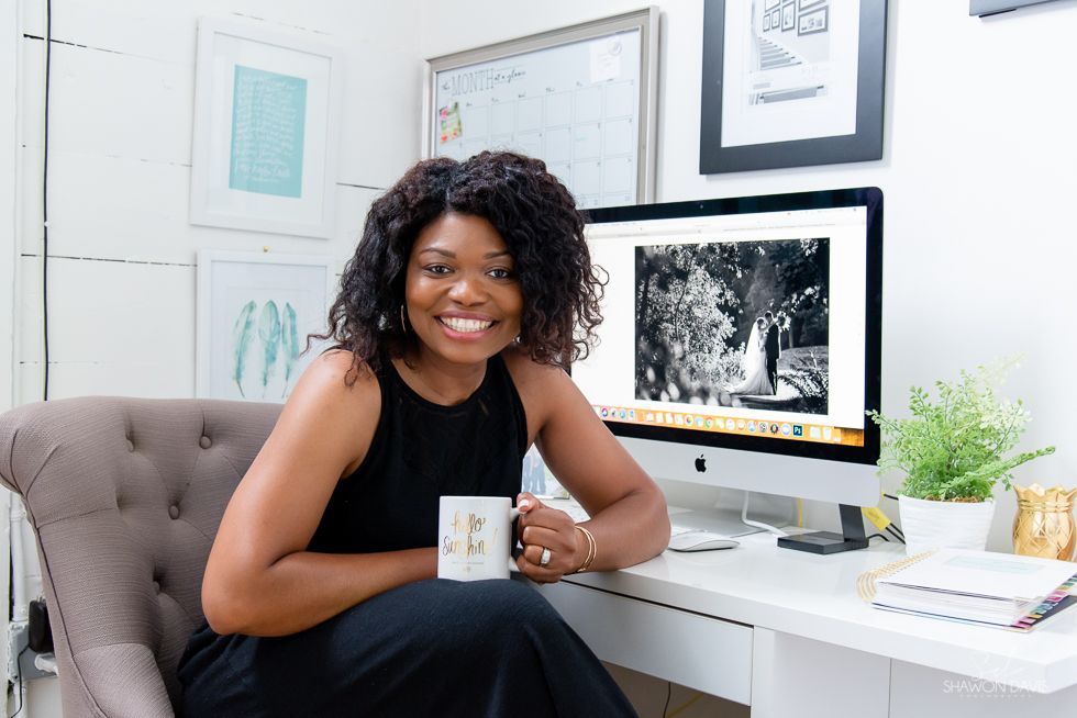 Woman smiling at a white desk with a mug, in a bright office with a computer and framed art.