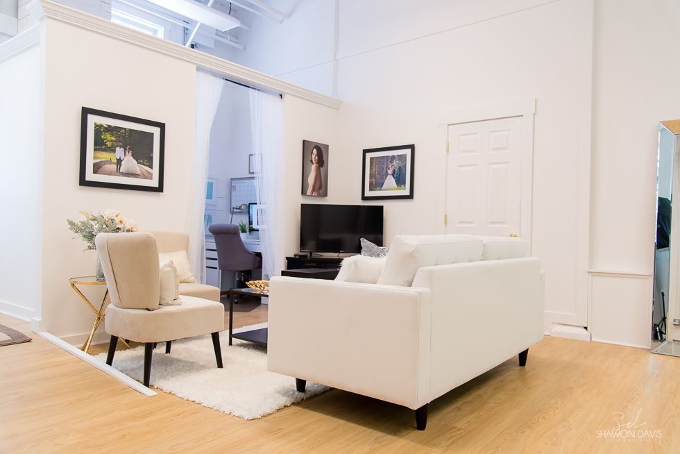 Bright living room with white sofa, beige chair, TV, and framed wall art on hardwood floors