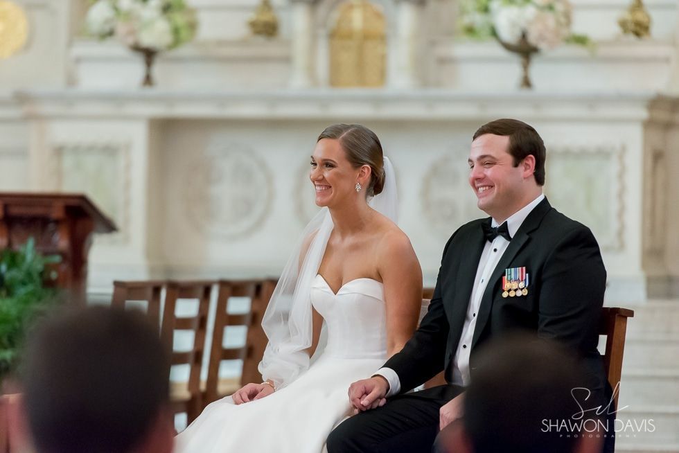 Bride and groom seated and smiling during a wedding ceremony in a decorated church.