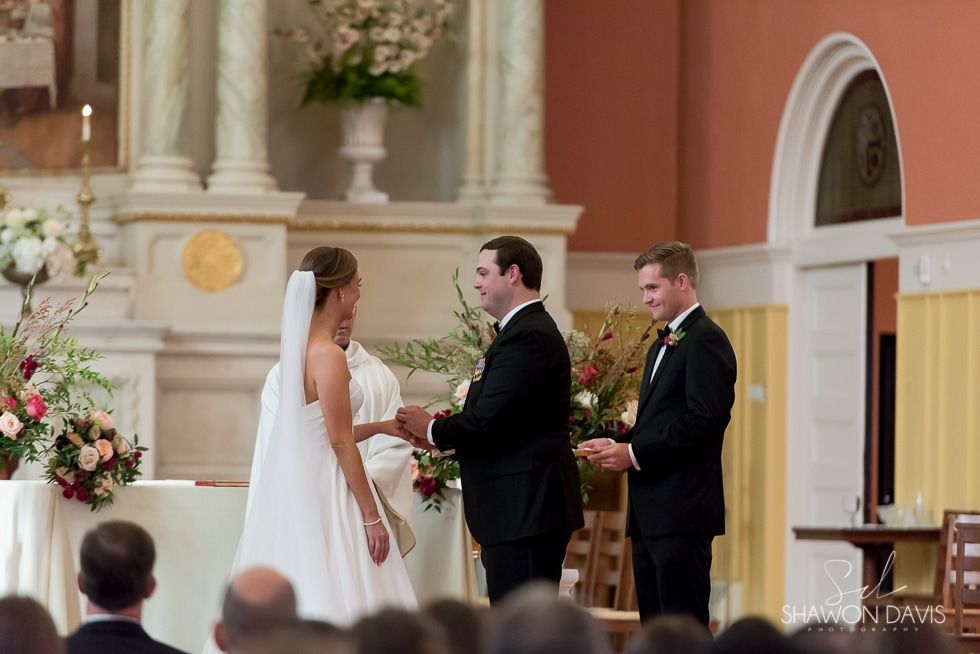 Wedding ceremony at the altar, bride in white facing groom in black suit as they exchange vows.