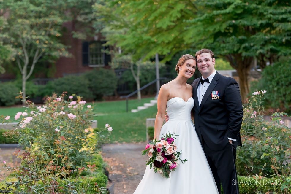Bride and groom posing in a garden, bride holding a bouquet and both smiling in wedding attire
