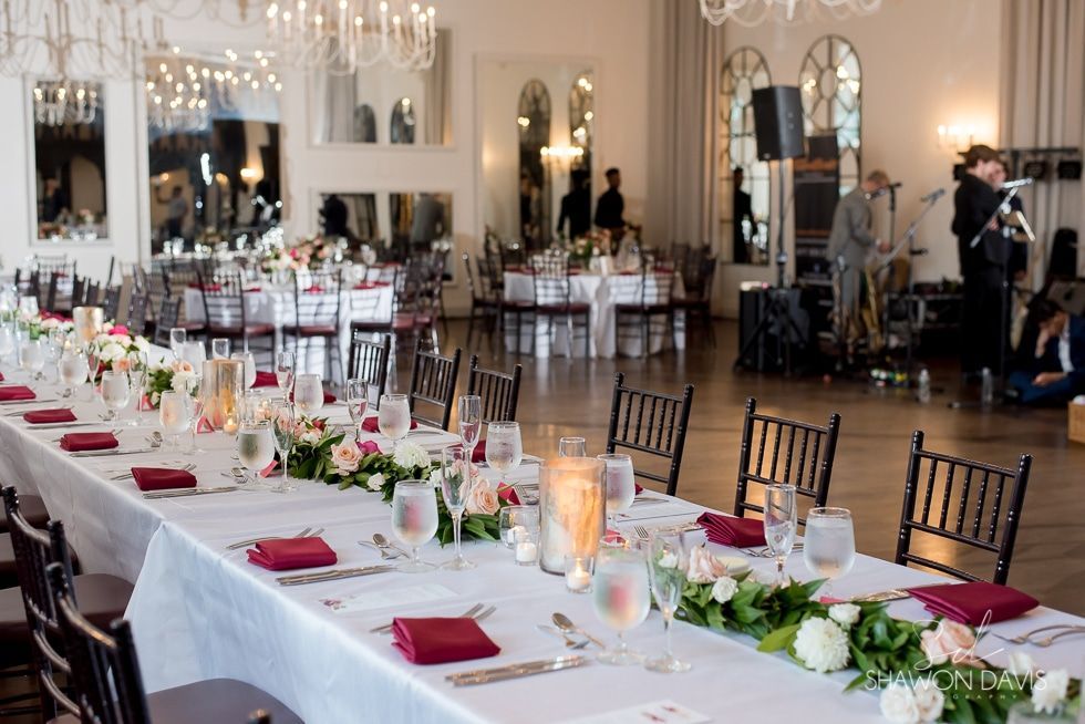 Elegant banquet hall with white-draped tables, red napkins, floral centerpieces, and chairs set for an event