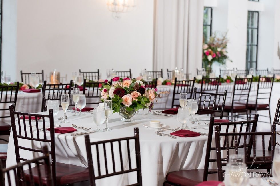 Round banquet tables set for an elegant event with white linens, red napkins, and floral centerpieces