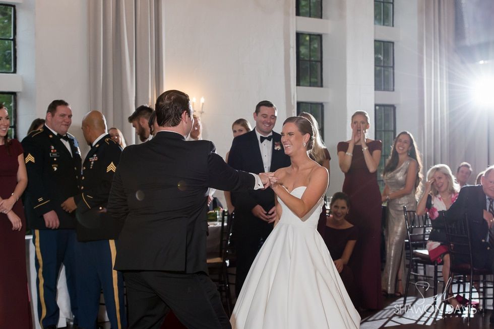 Bride and groom dancing at a formal indoor reception, guests applauding nearby