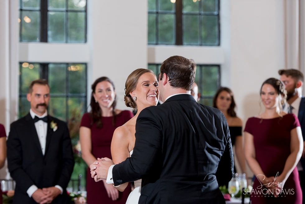 Bride and groom dance at a wedding reception while bridesmaids and groomsmen watch nearby.