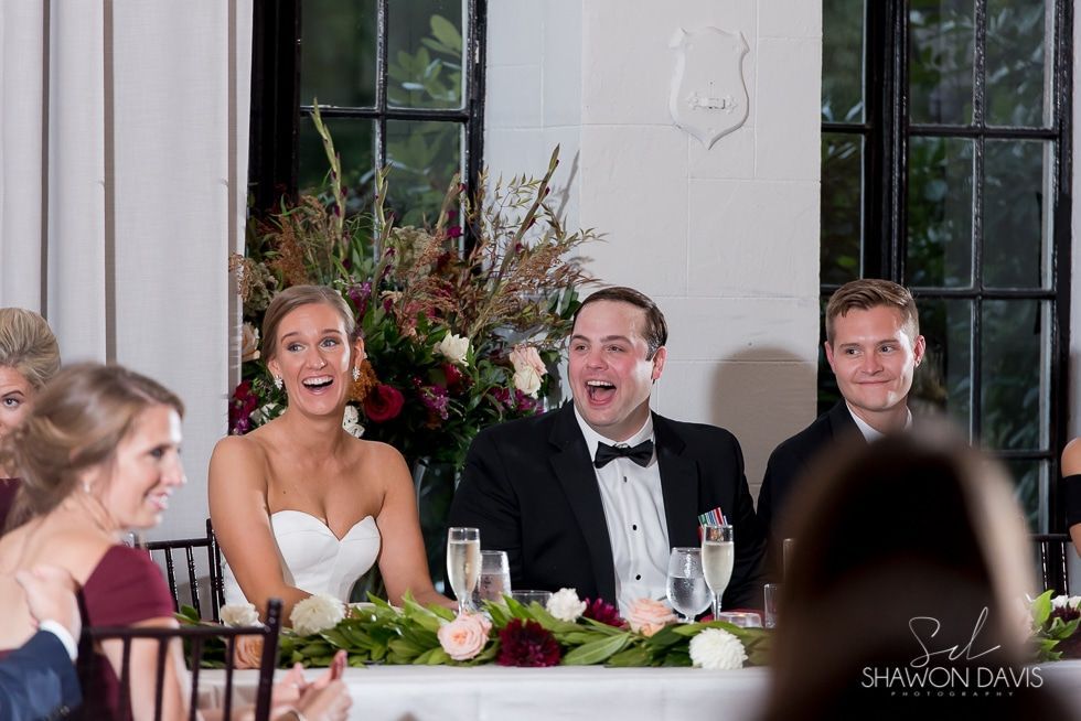 Wedding guests seated at a reception table, laughing and smiling in formalwear