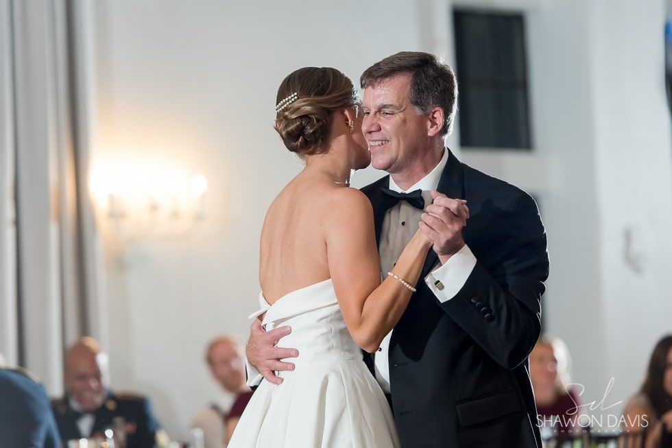 Couple dancing closely at a formal indoor wedding reception, smiling in a white gown and black tuxedo