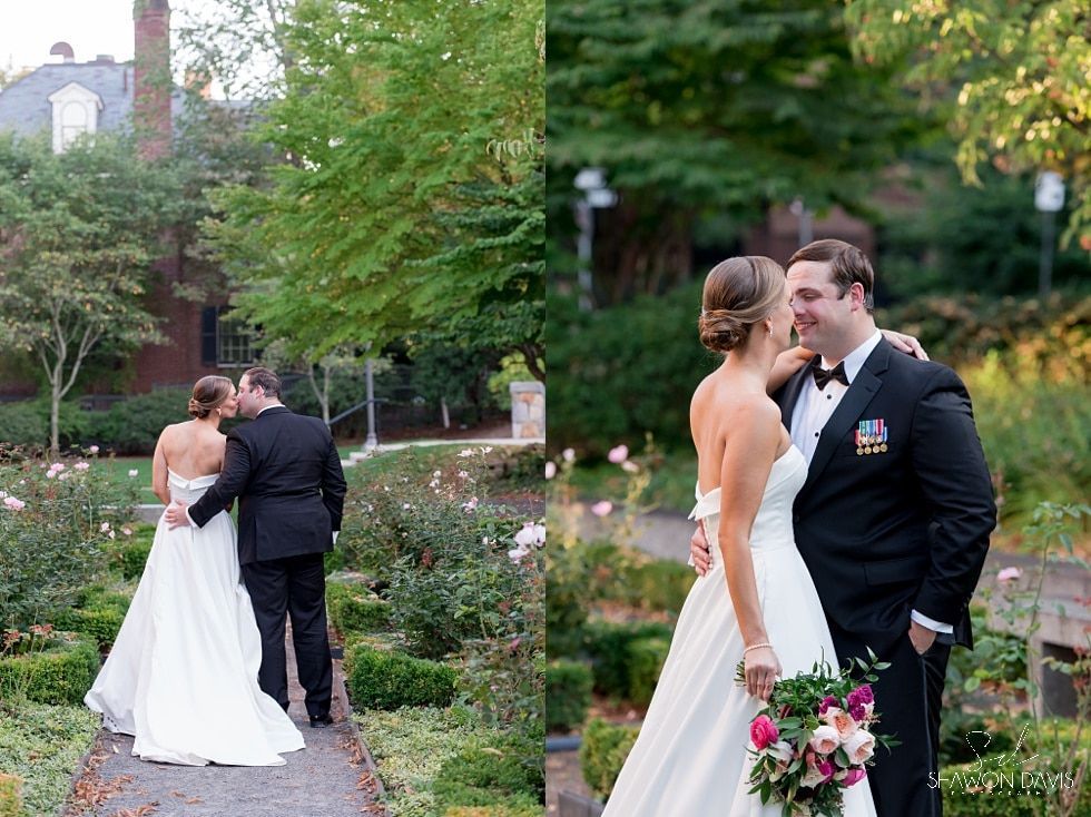 Wedding couple posing in a garden, bride in white dress holding bouquet, groom in dark military uniform.
