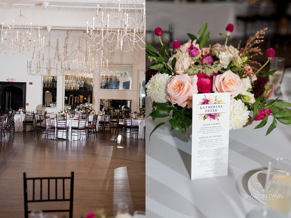 Floral arrangement on a table in a bright, elegant banquet hall with chandeliers and set dining tables