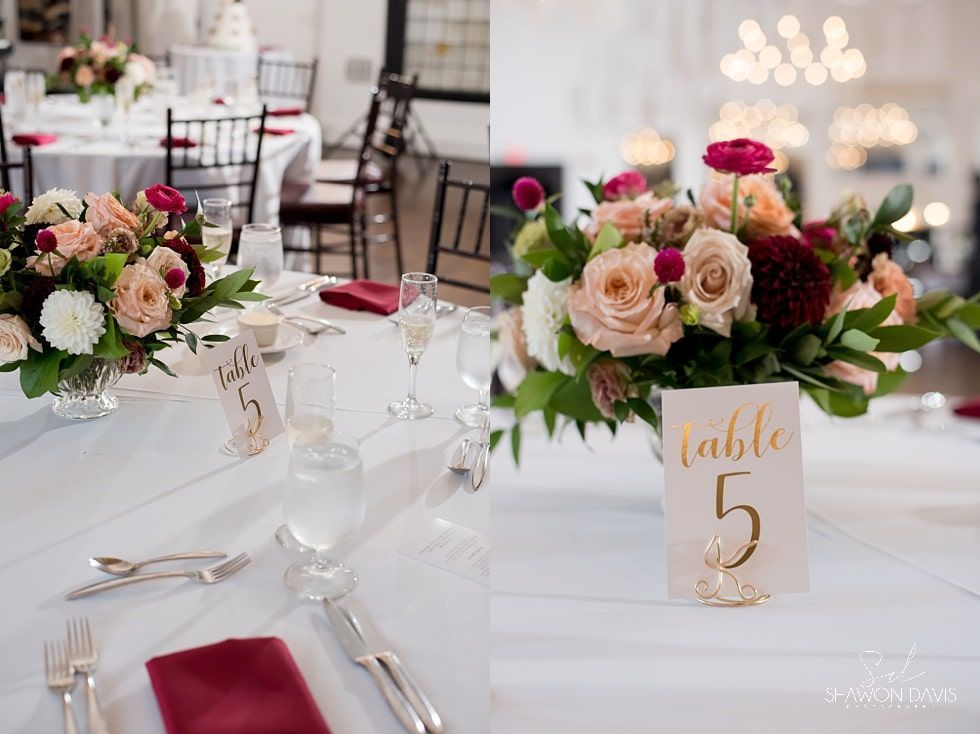 Elegant wedding reception table with pink and white floral centerpieces, folded napkins, and table number 5