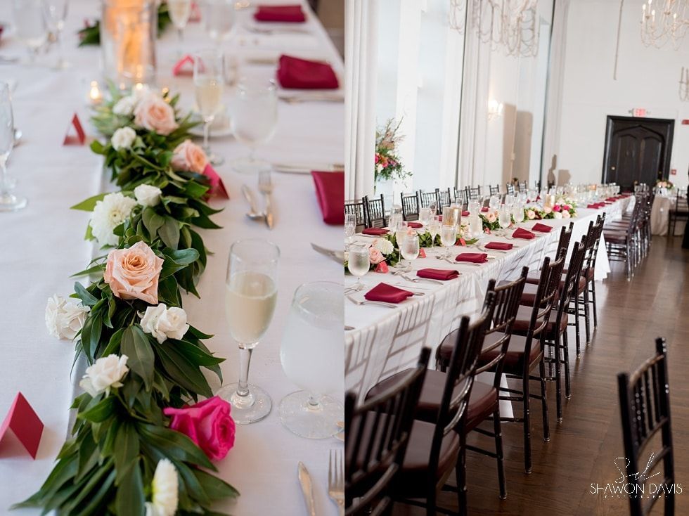 Elegant long banquet table with white linens, burgundy napkins, candles, and floral arrangements by a bright window