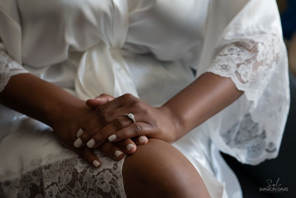 Hands resting in lap, wearing a white lace robe and silver rings.