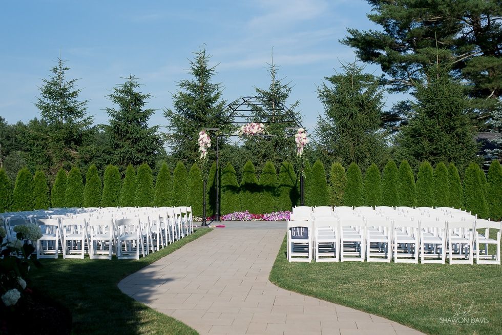 Outdoor wedding setup with white chairs lining a garden path in a green park.