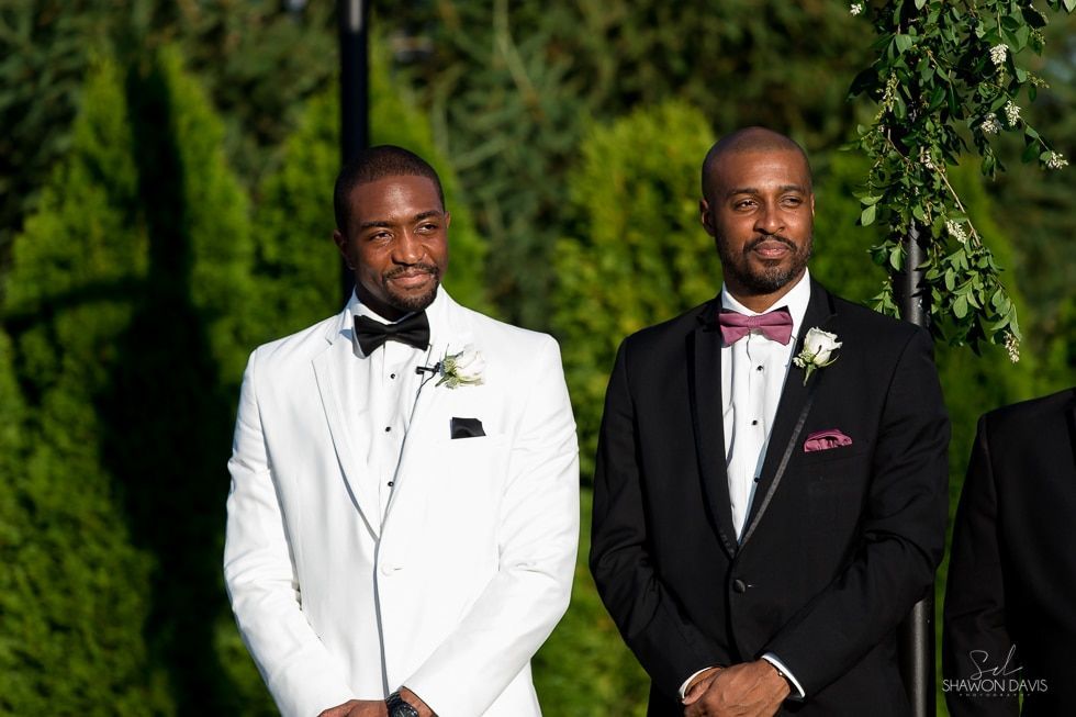 Two men in formal suits standing outdoors at a wedding