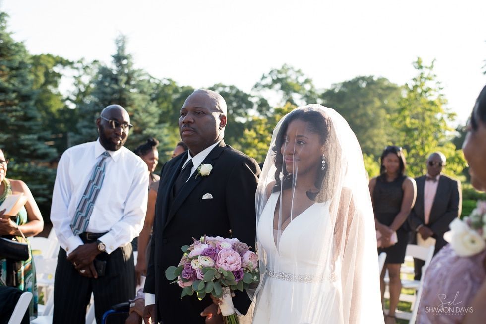 Outdoor wedding ceremony with bride in white veil and groom in black suit holding a bouquet