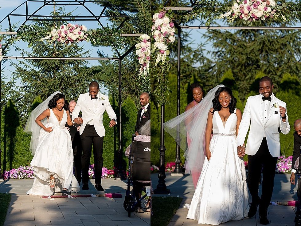 Wedding party walking down an outdoor aisle beneath floral archways at a garden ceremony