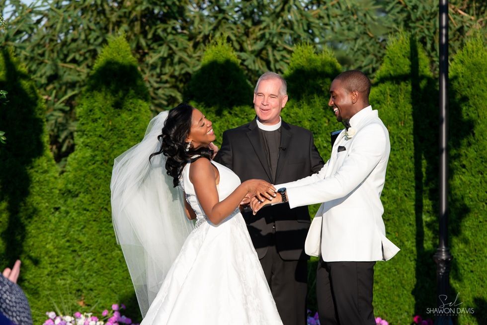 Bride and groom holding hands during outdoor wedding ceremony, with officiant behind them.