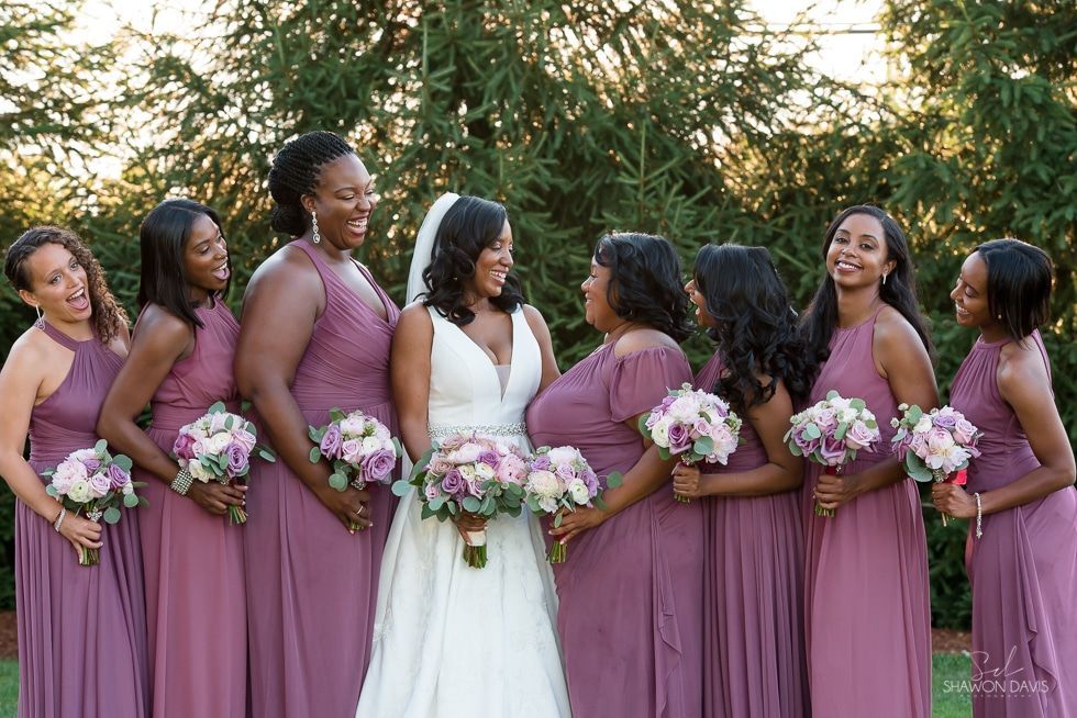 Bride and bridesmaids in mauve dresses holding bouquets outdoors in a garden ceremony