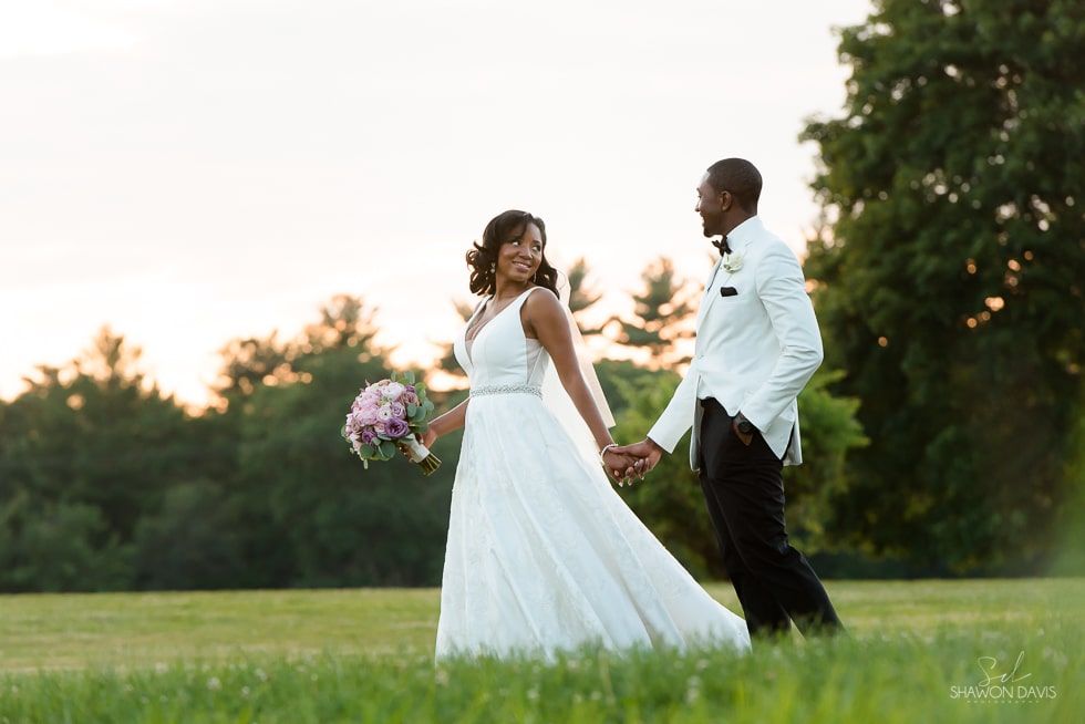 Bride and groom walking hand in hand in a grassy field at sunset
