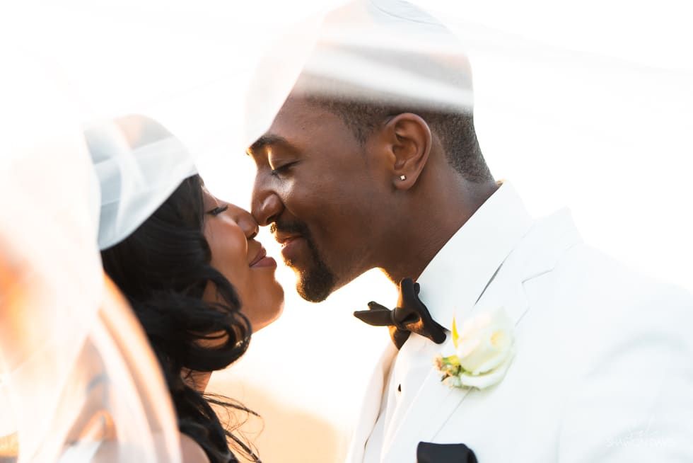 Two brides in white wedding attire sharing a close, joyful kiss outdoors