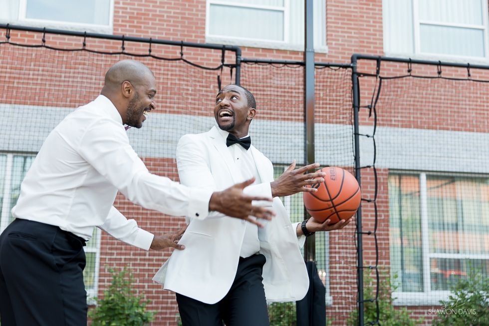 Two men in white blazers playing basketball and smiling on an outdoor court