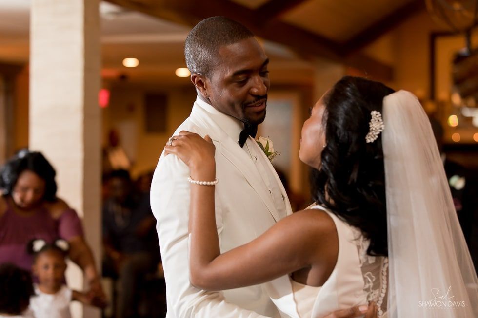 Wedding couple dancing closely at the reception, the bride in a white dress and veil, warmly smiling.