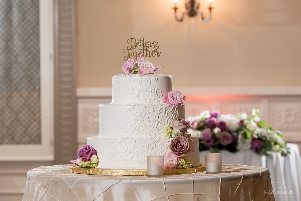 Three-tier white wedding cake with pink flowers on a decorated reception table