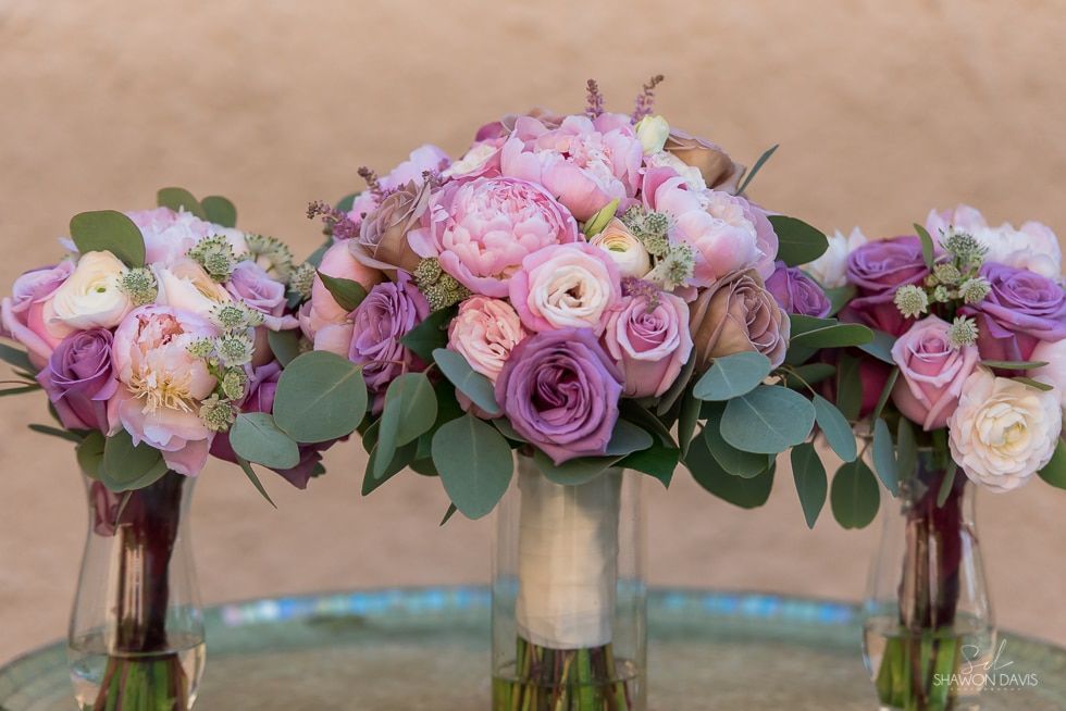 Three pink and purple floral arrangements in glass vases on a table