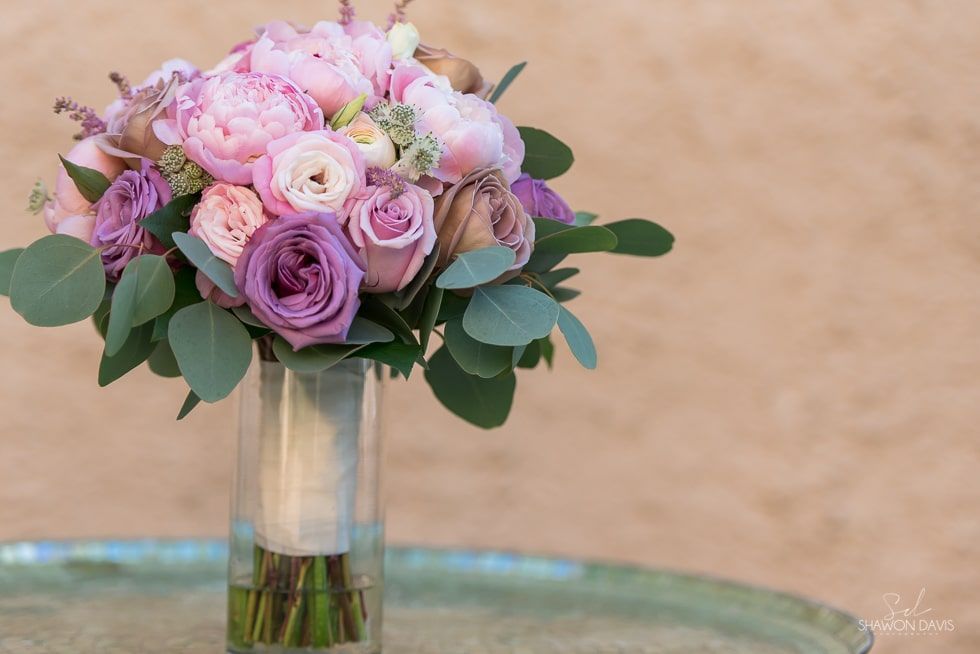 Pink and lavender rose bouquet in a clear glass vase against a beige background