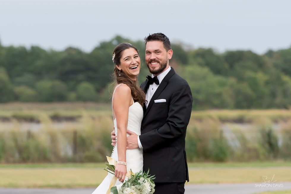 Bride and groom smiling outdoors in a field, with trees in the background