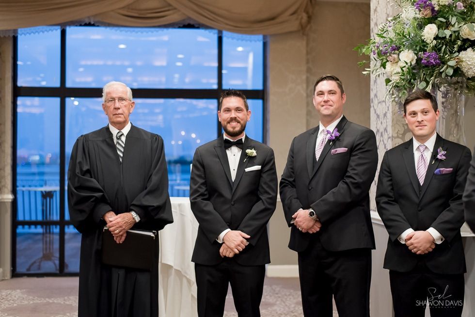 Four people in black formal attire standing together indoors at an event.