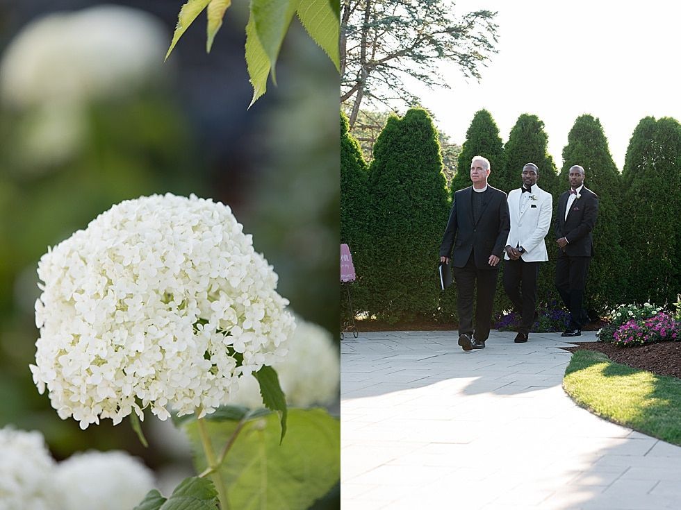 Three people walking along a garden path beside white flowers and trimmed hedges