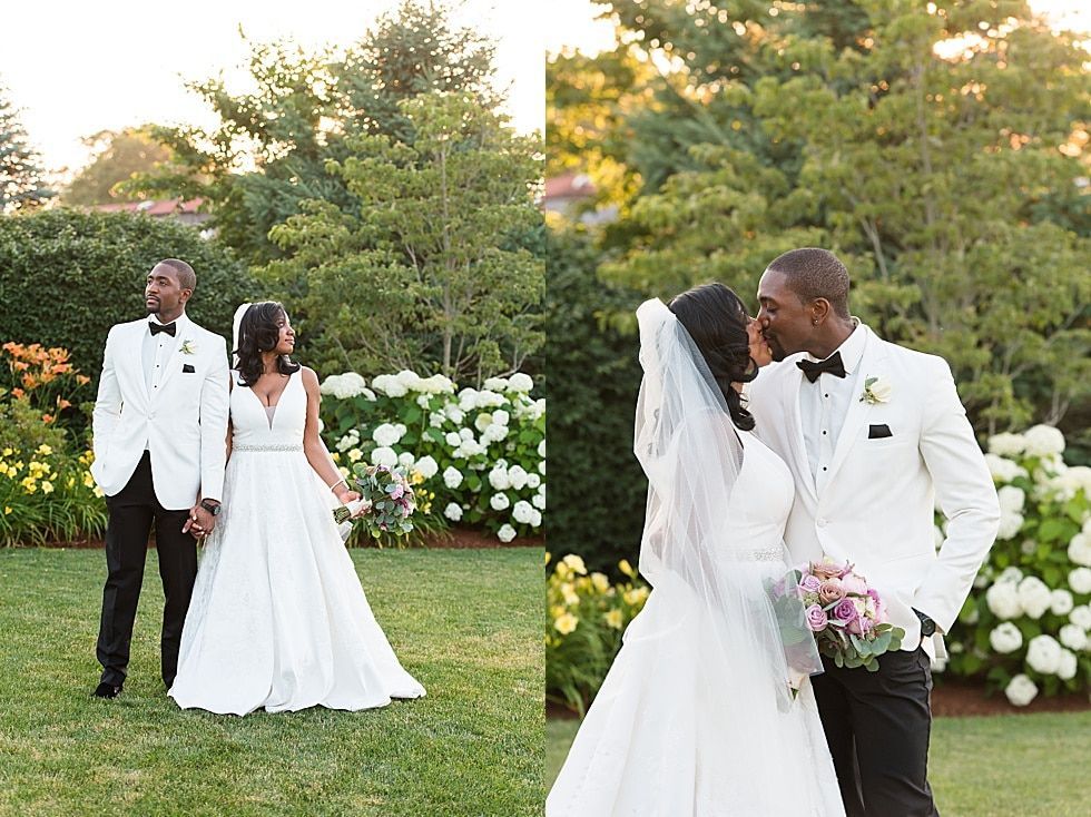 Couple in white wedding attire standing in a garden, with another couple nearby and white flowers behind them