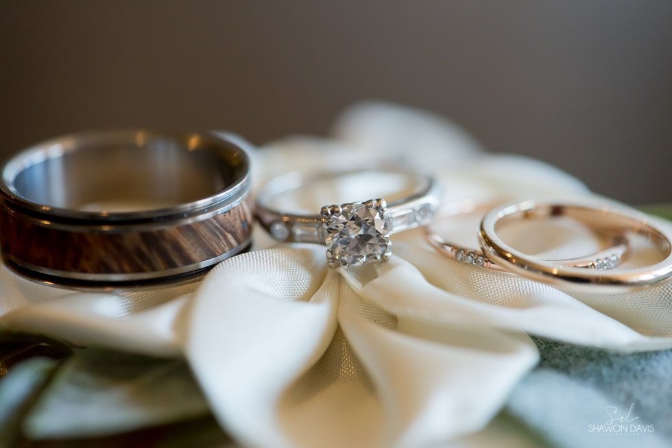 Three wedding rings resting on white petals, including a diamond engagement ring and a gold band.