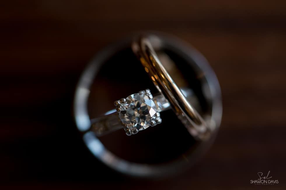 Two intertwined silver rings with a diamond engagement ring on a dark wooden surface