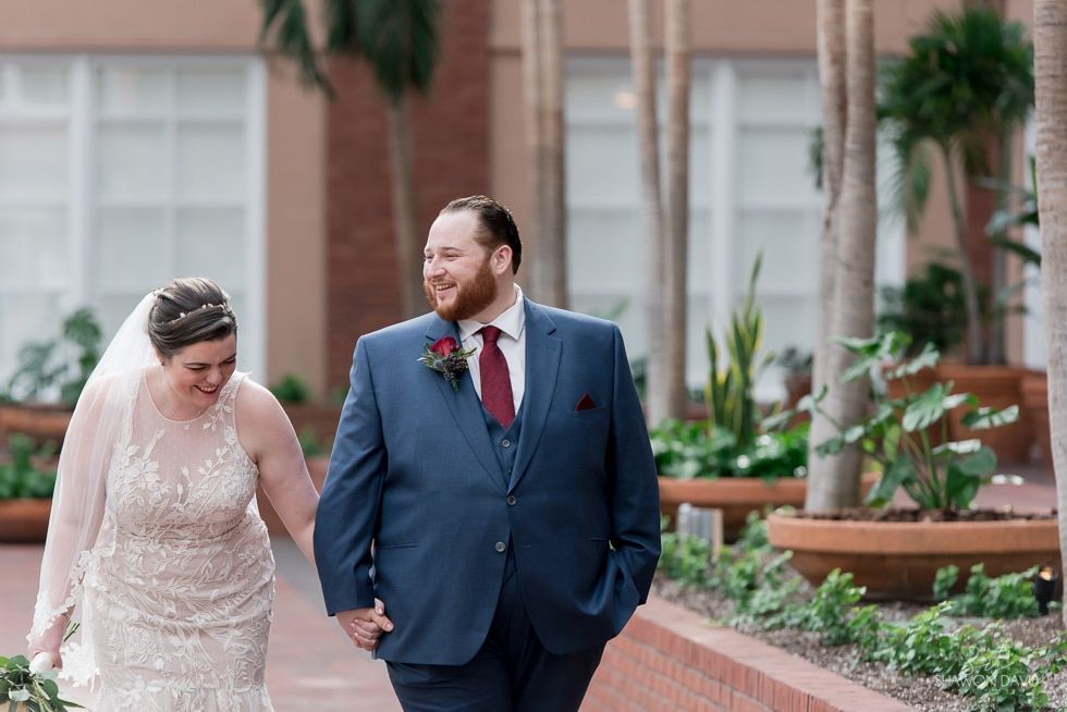 Bride and groom walking together in a garden courtyard, smiling and holding hands
