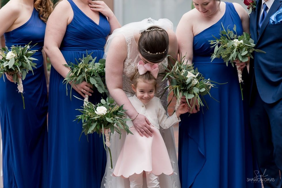 Bride bending to hug a little girl among bridesmaids in blue dresses holding bouquets