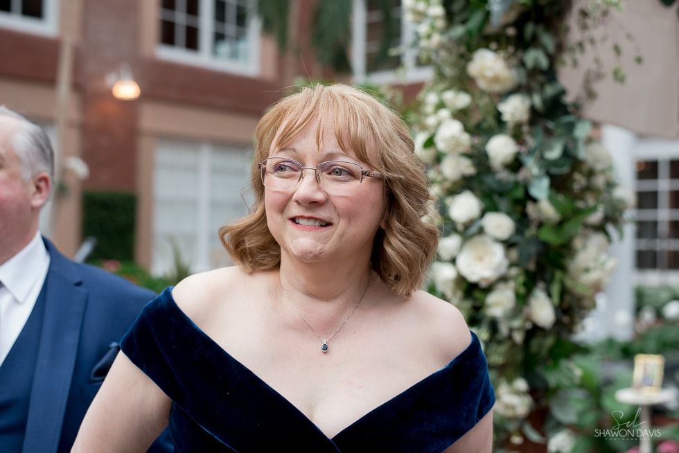 Smiling woman in a navy off-shoulder dress at an outdoor event with white floral decorations