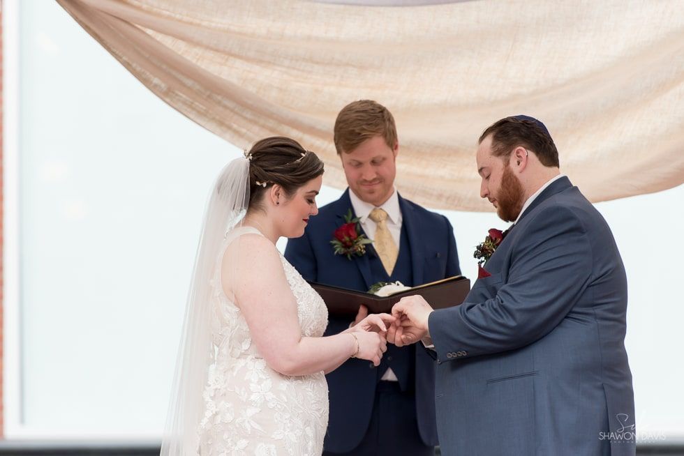 Wedding ceremony with couple exchanging rings before an officiant under a white draped canopy