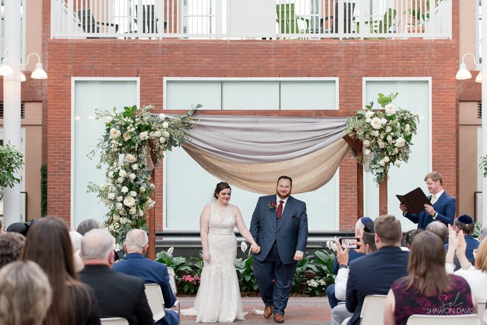 Wedding ceremony under floral arch with couple standing together and guests seated in front