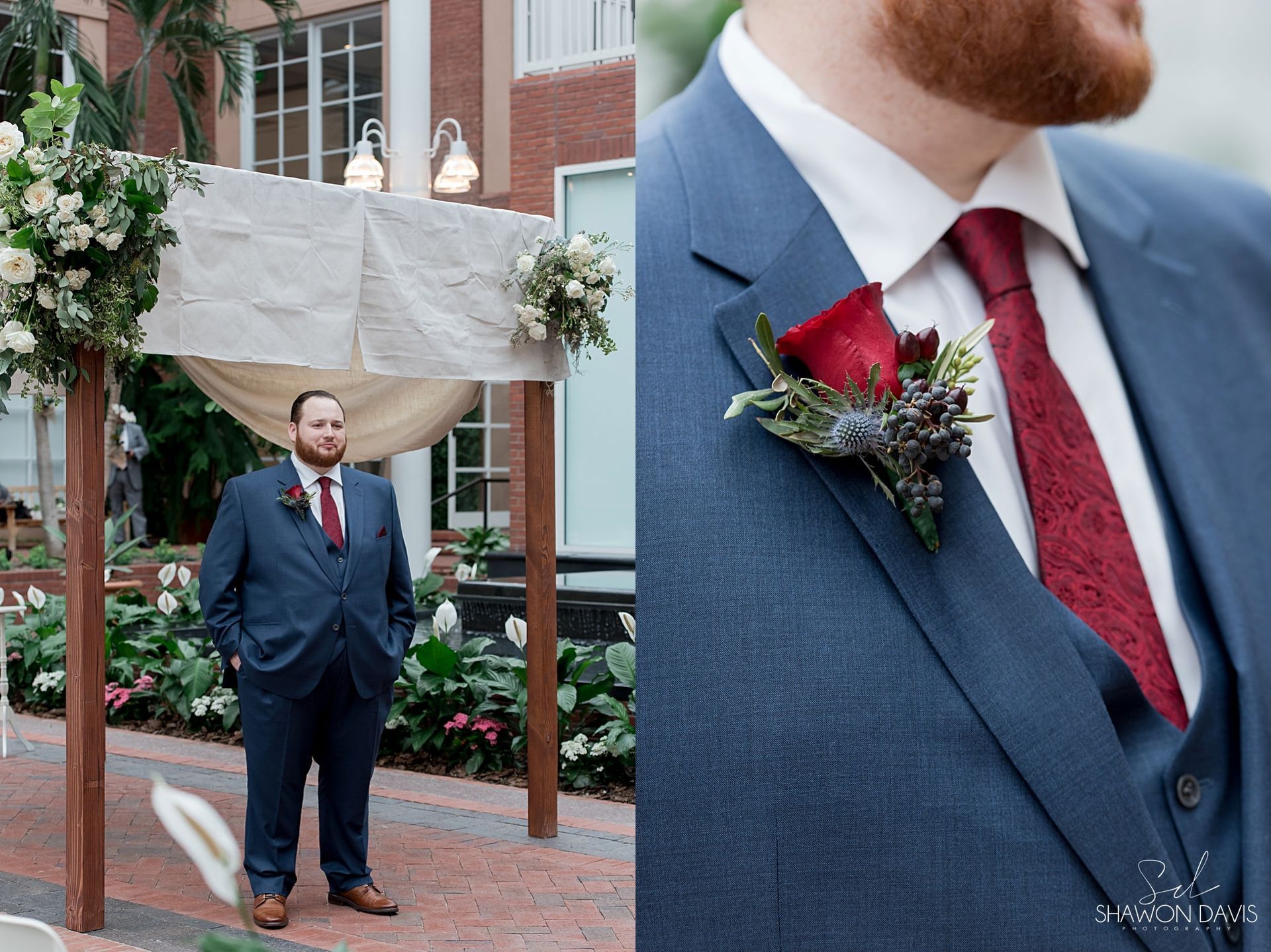 Man in navy suit and red tie standing beside a flower-covered wedding arch outdoors