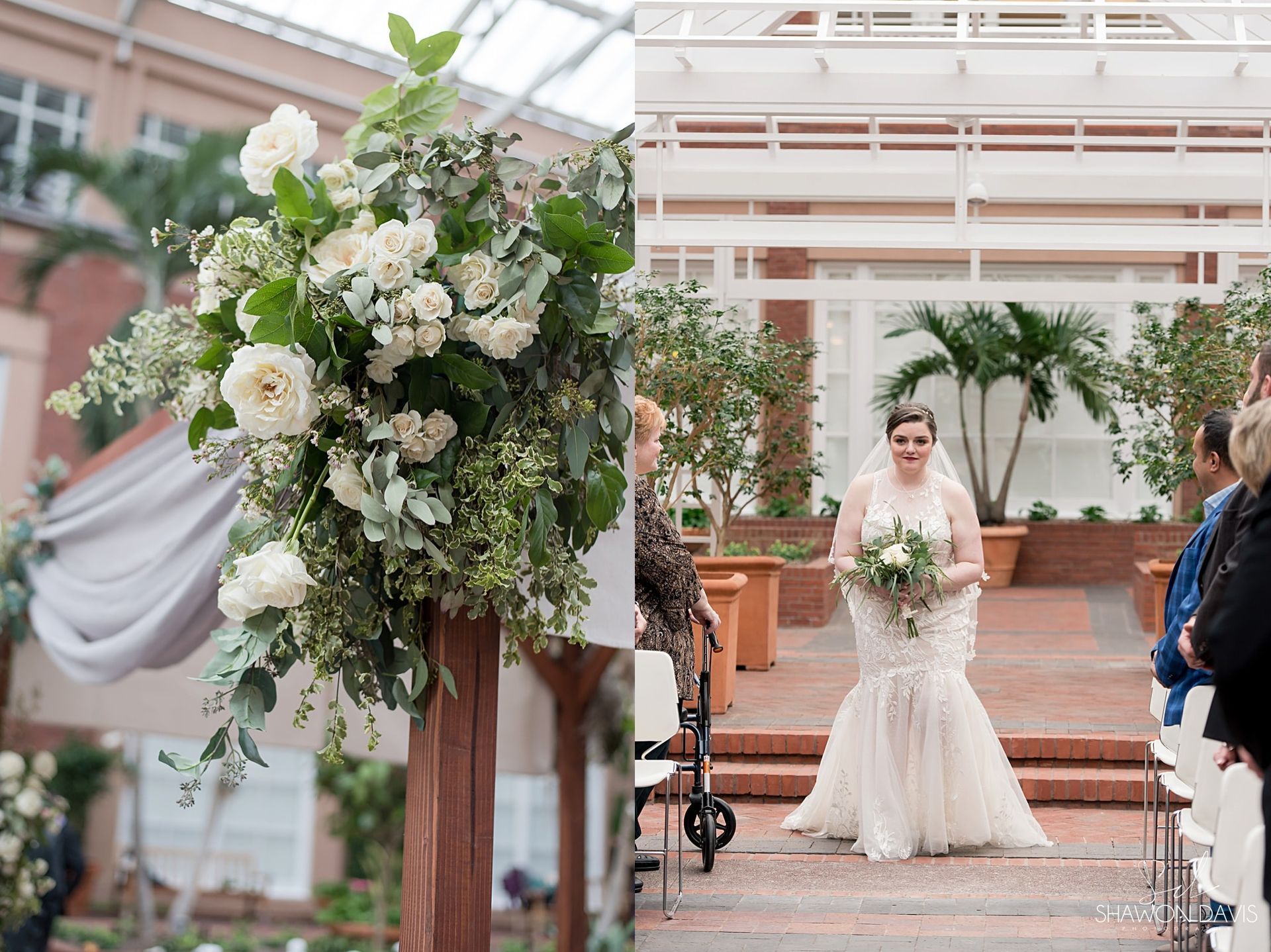 Bride in white gown holding bouquet at an outdoor wedding ceremony, beside a large floral arrangement.