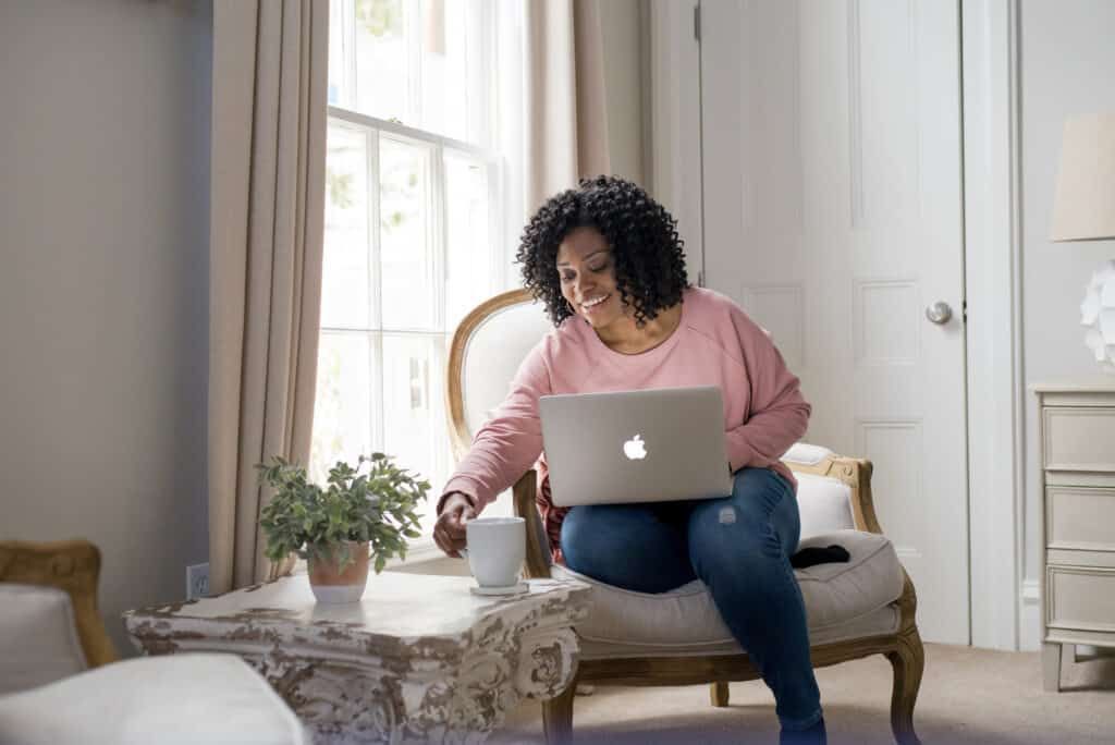 Woman sitting on a sofa using a laptop beside a coffee table in a bright living room